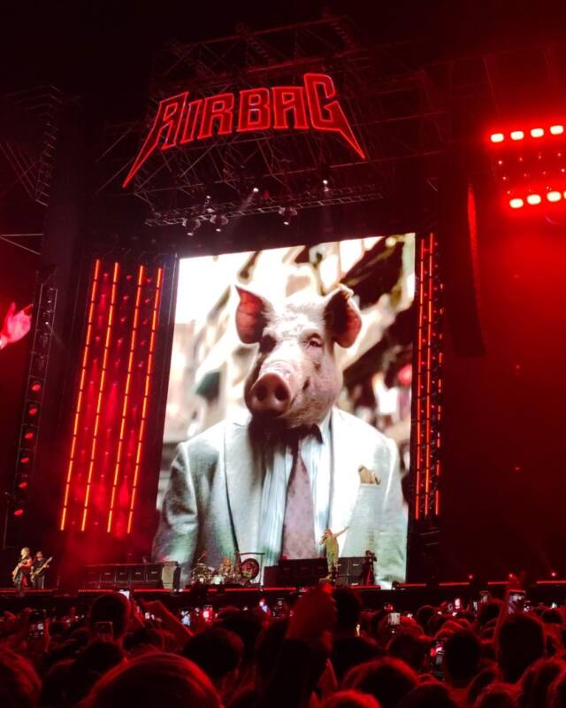 Imagen del escenario de Airbag en River con una proyección en la pantalla de una persona que viste un traje y tiene cabeza de cerdo.
